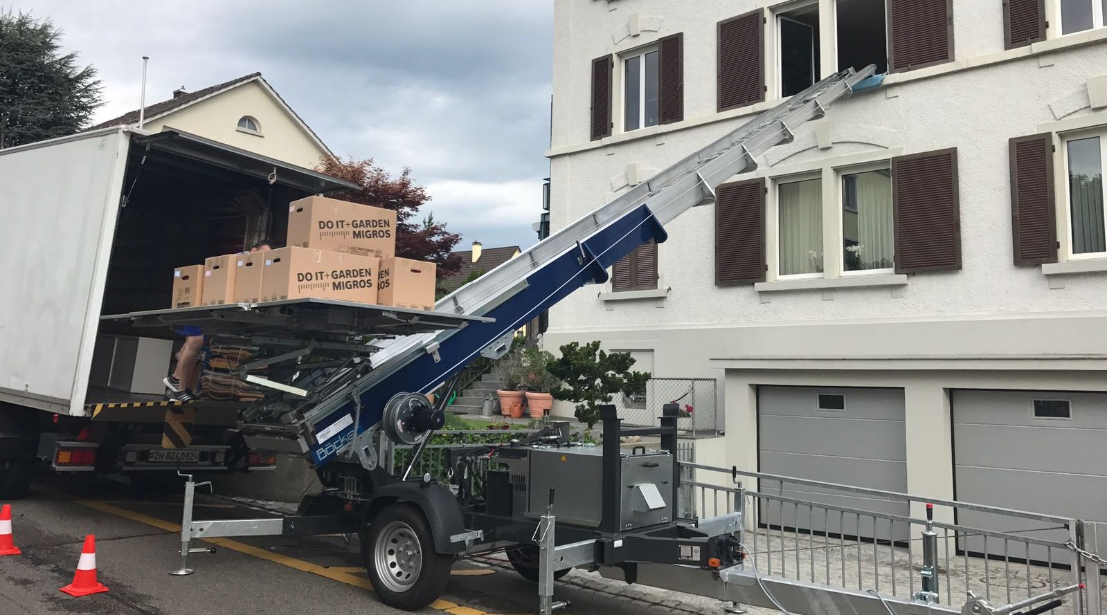 Lkw mit Umzugslift und Kartons, die für einen Umzug in Zürich bereitgestellt werden, vor einem mehrstöckigen Wohnhaus.