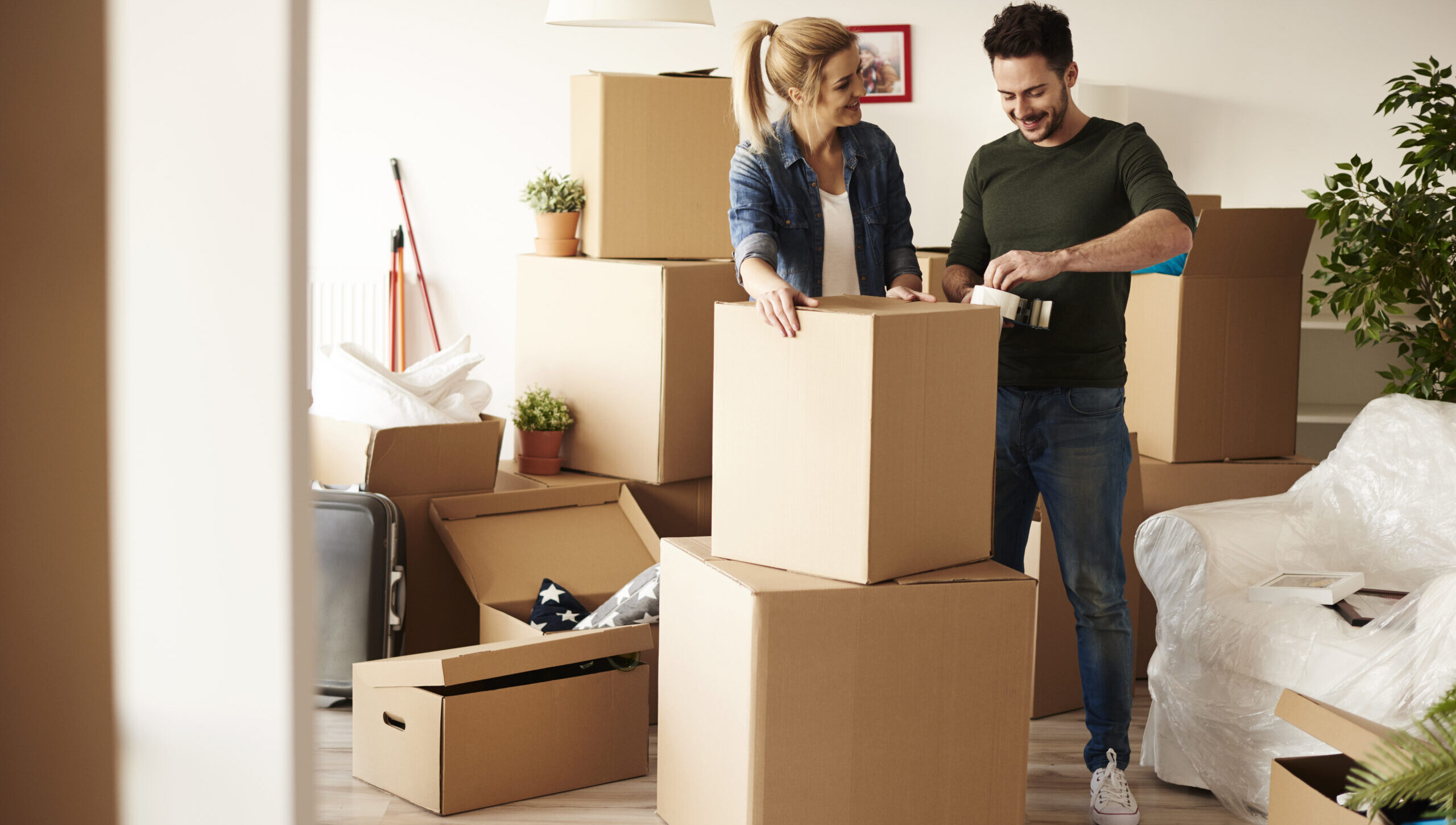 Paar beim Packen von Umzugskartons in einem Wohnzimmer, umgeben von weiteren Kartons, symbolisiert stressfreies Umziehen und professionelle Umzugsdienstleistungen in Zürich.